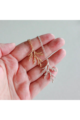 Juniper branch necklace by Birch Jewellery; shown held in a hand, in silver and gold
