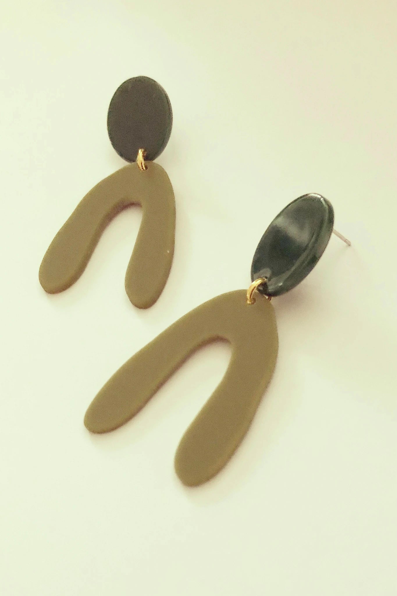 Kuvve dangle earrings by Darlings of Denmark; olive green arches hanging off a black oval shape; geometric, graphic earrings; acrylic acetate and raw brass; flat lay