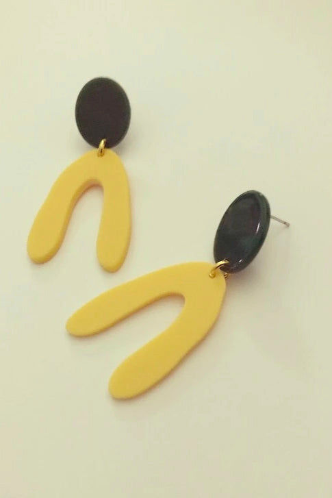 Kuvve dangle earrings by Darlings of Denmark; yellow arches hanging off a black oval shape; geometric, graphic earrings; acrylic acetate and raw brass; flat lay