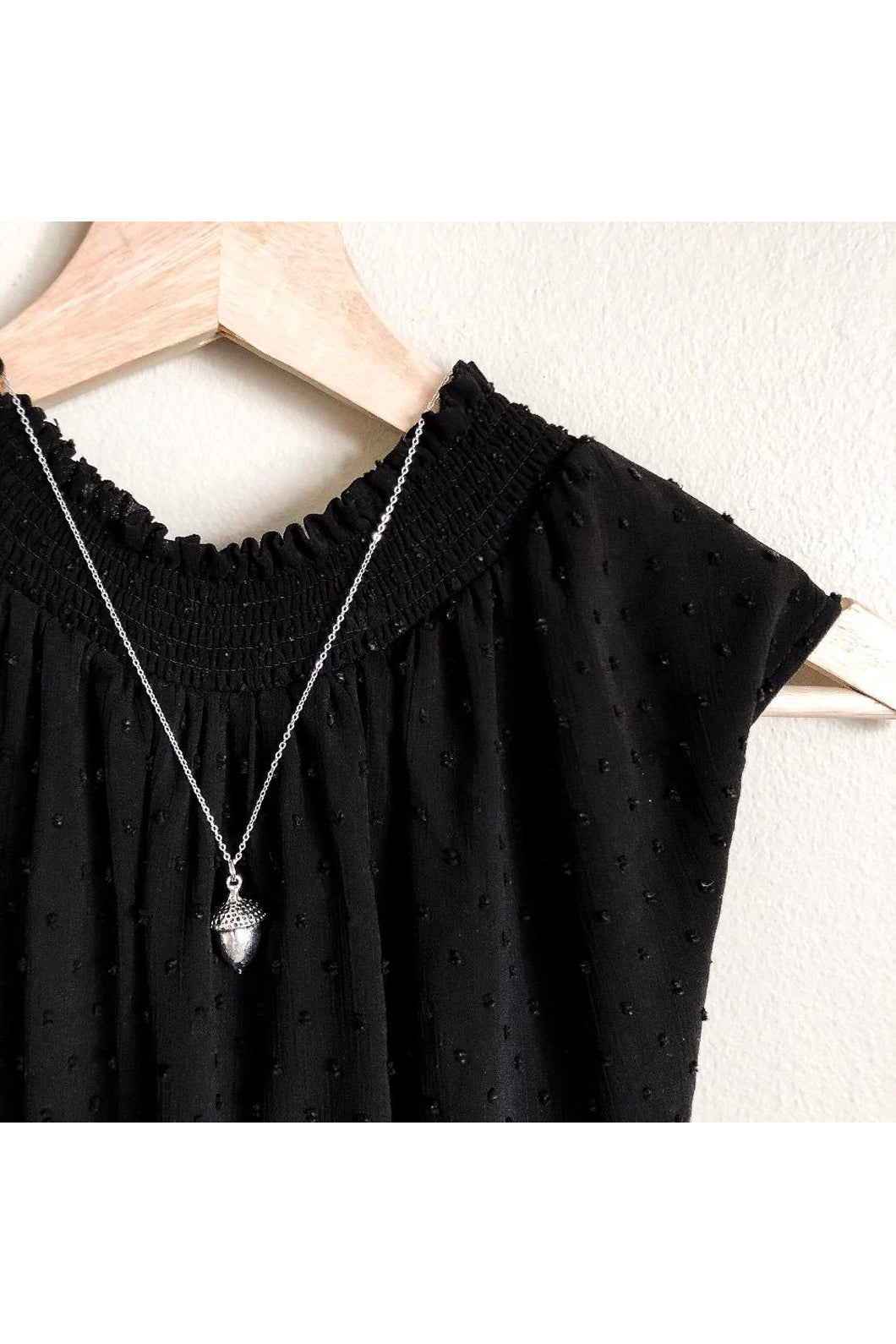 Large acorn necklace by Birch Jewellery; shown in silver; flat lay; styled on a black top on a wooden hanger
