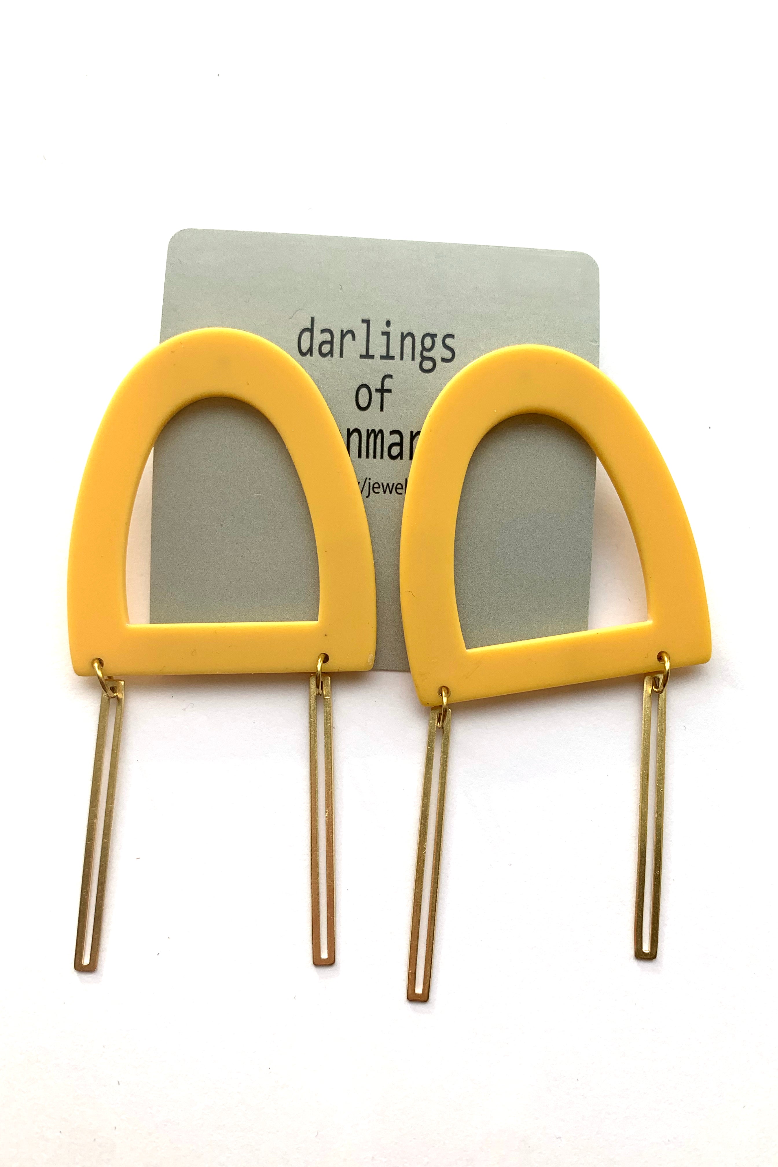 Lily earrings by Darlings of Denmark; large stud earrings with hollowed, acrylic, yellow geometric shape, and dangling raw brass sticks; flat lay
