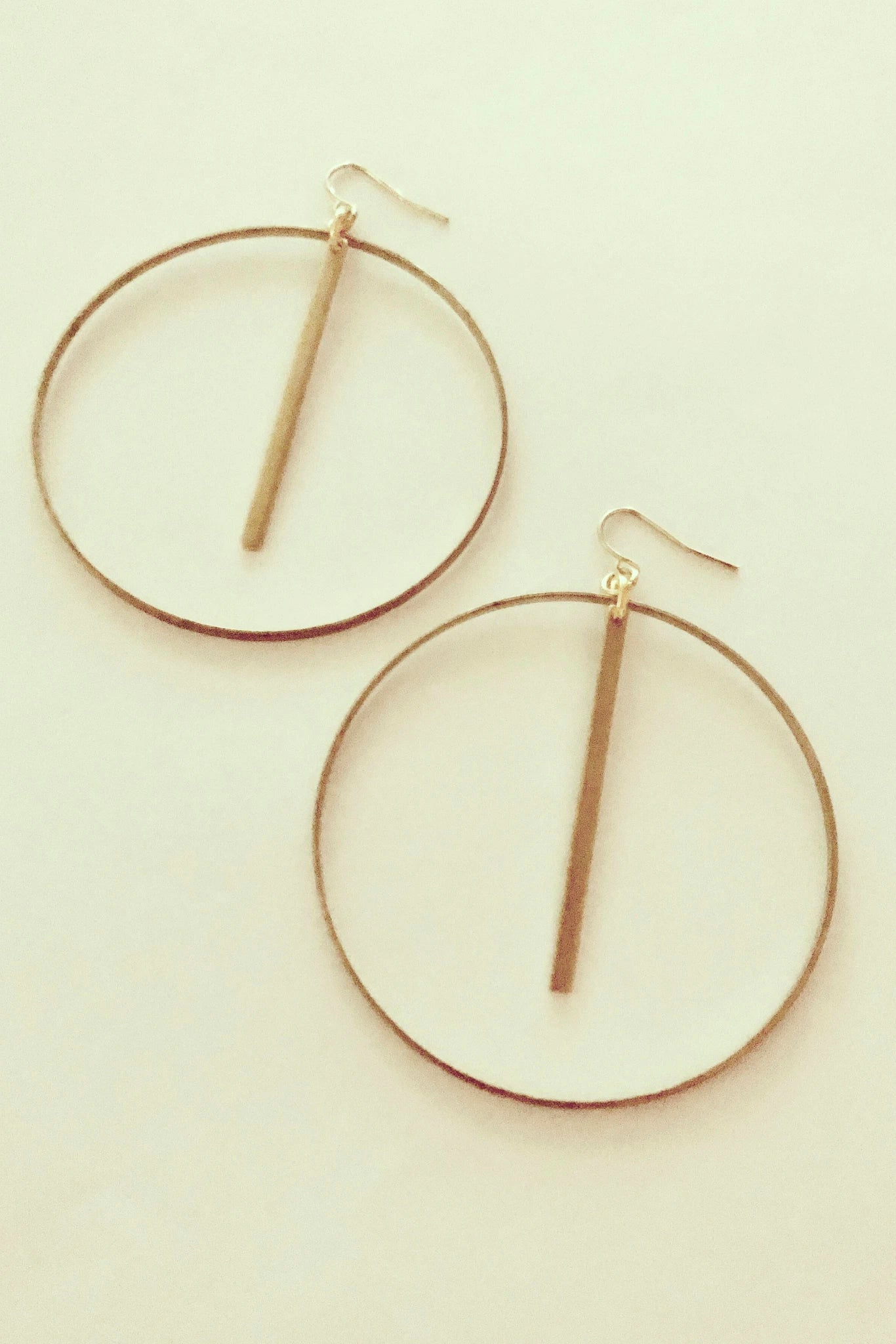 Myne by Darlings of Denmark; large, thin hoops with a hanging stick; raw brass; flat lay