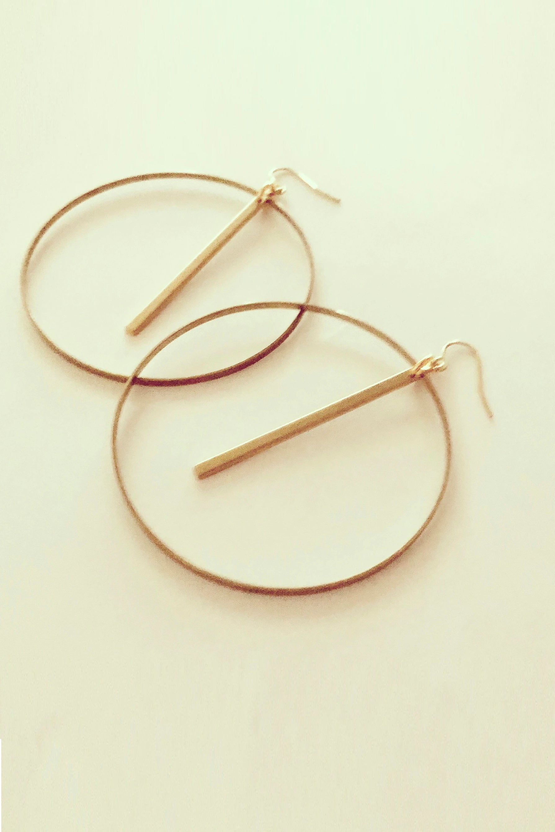 Myne by Darlings of Denmark; large, thin hoops with a hanging stick; raw brass; flat lay